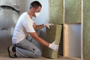 Worker in protective goggles and respirator insulating rock wool